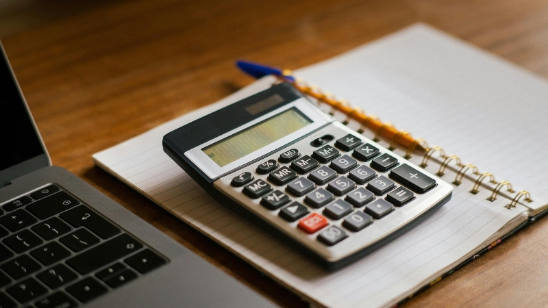 Kalkulator i sveska na stolu simbolično prikazuju svakodnevne knjigovodstvene obaveze u poslovanju jednog DOO preduzeća